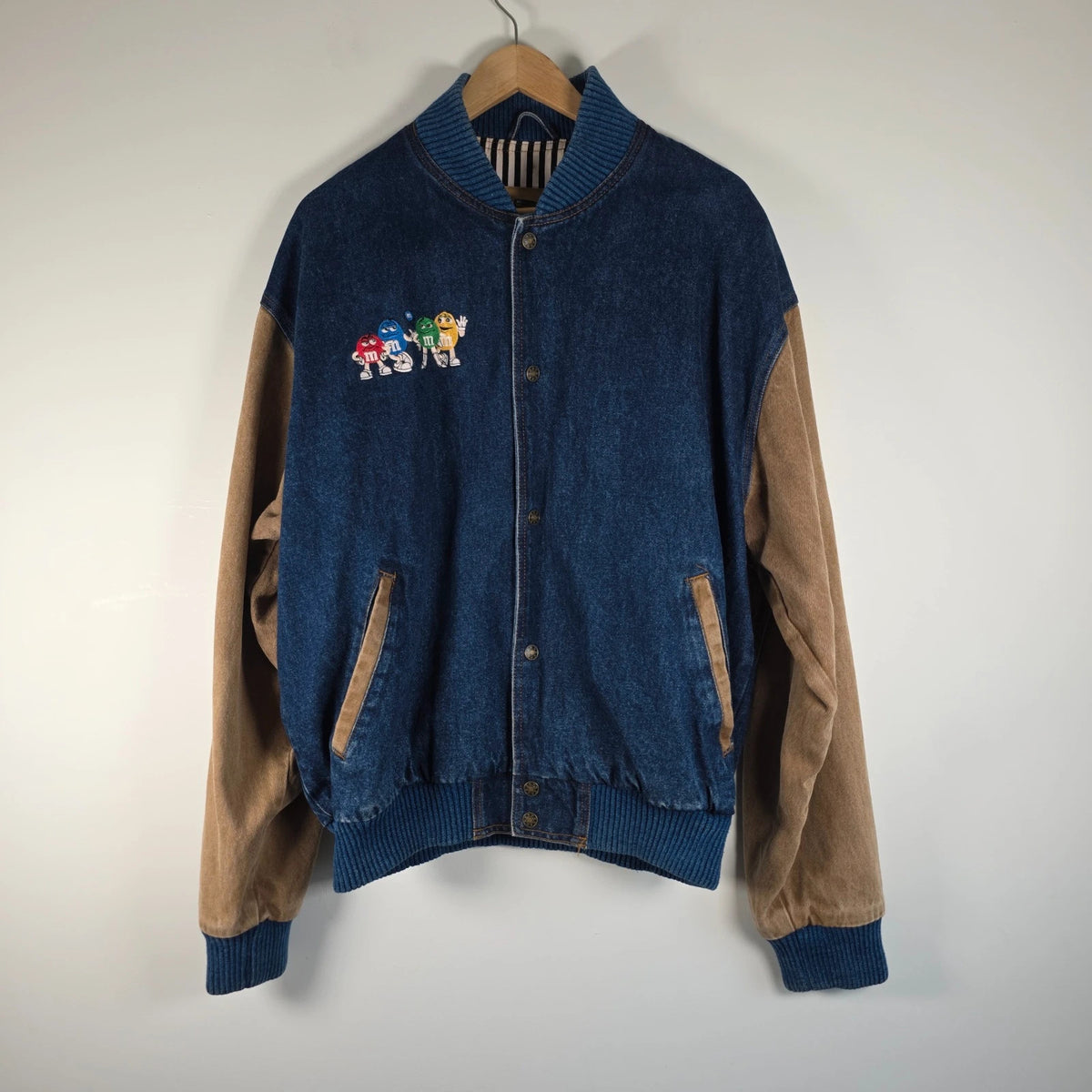 M&M's blue denim varsity bomber jacket with embroidered characters and tan sleeves.