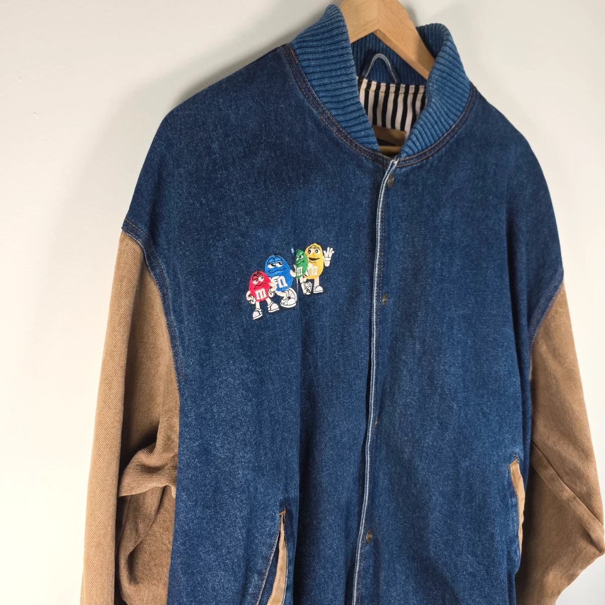 M&M's blue denim varsity bomber jacket with embroidered characters and tan sleeves.