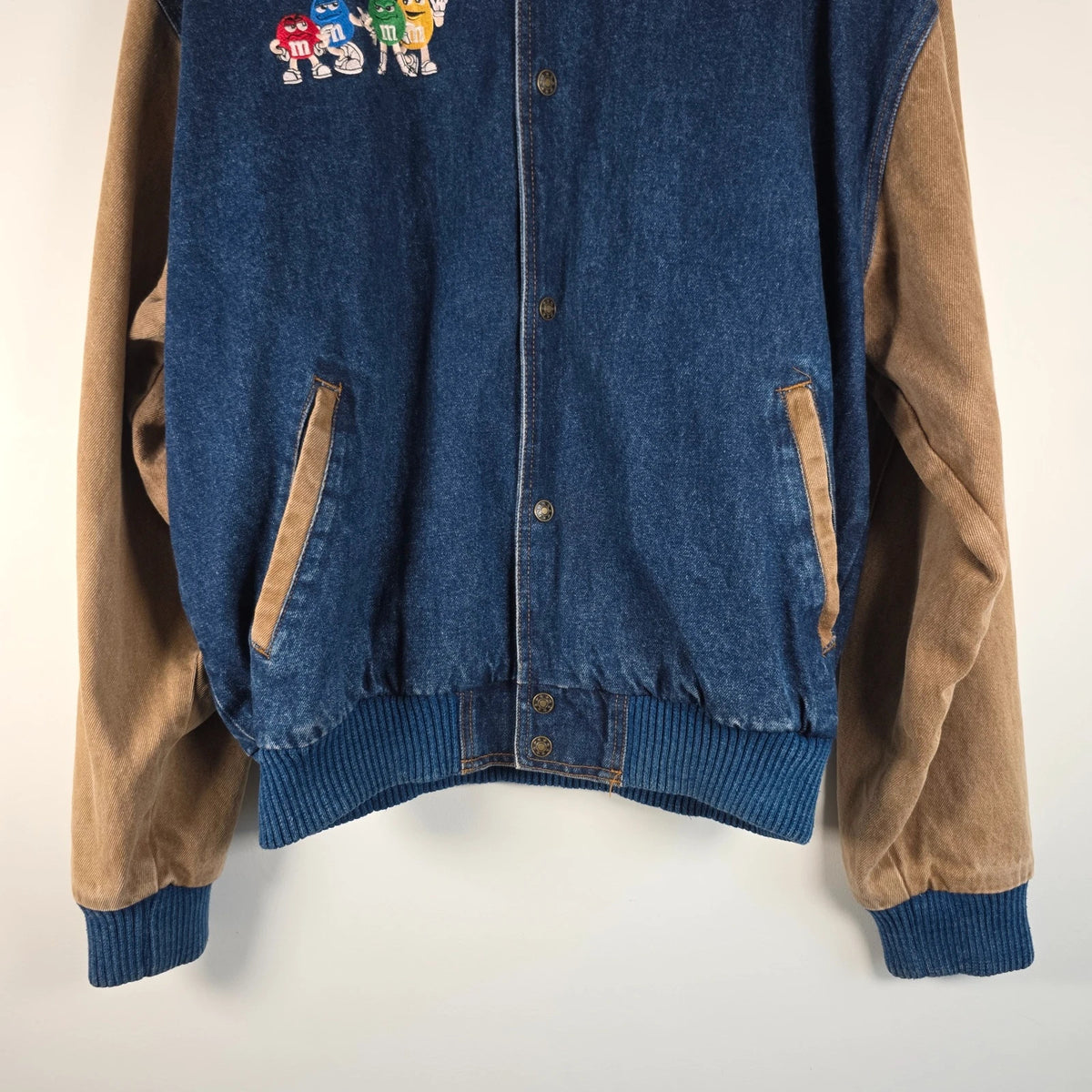 M&M's blue denim varsity bomber jacket with embroidered characters and tan sleeves.