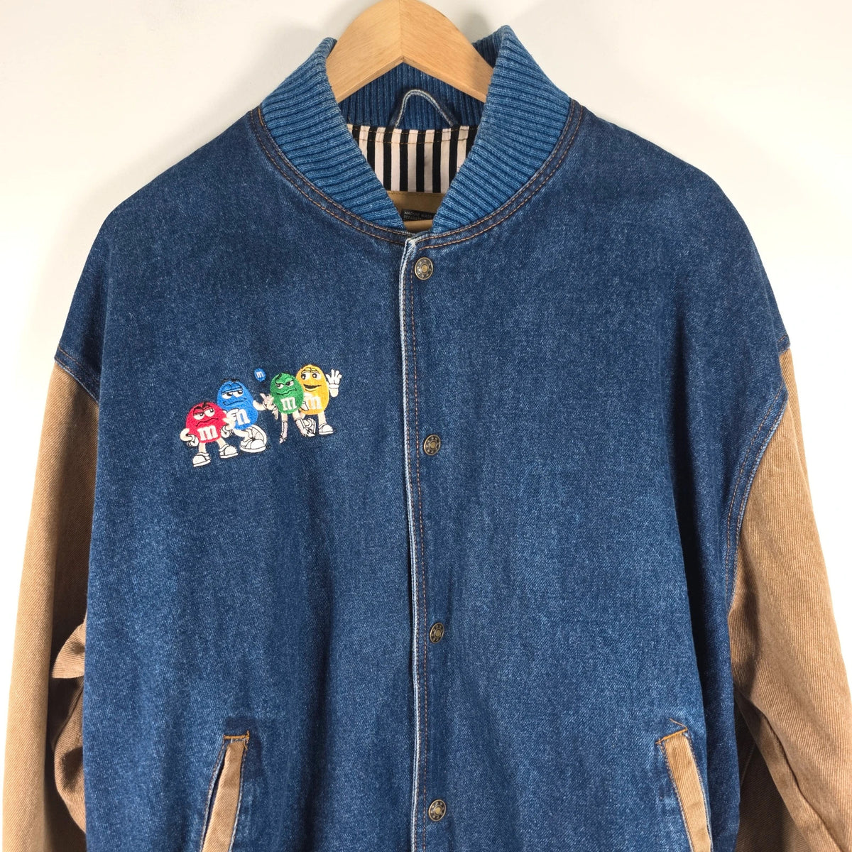 M&M's blue denim varsity bomber jacket with embroidered characters and tan sleeves.