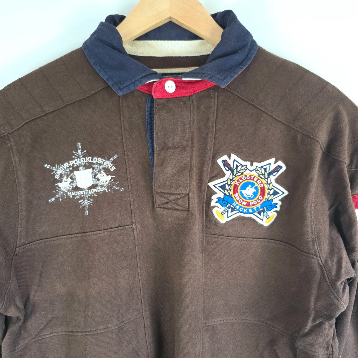 Hackett brown rugby polo shirt with navy collar, embroidered patches, and large back design.