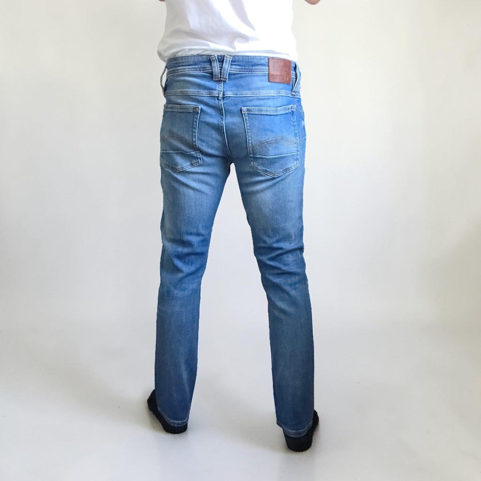 Tommy Hilfiger blue tapered jeans with stretch denim and small rip detail.