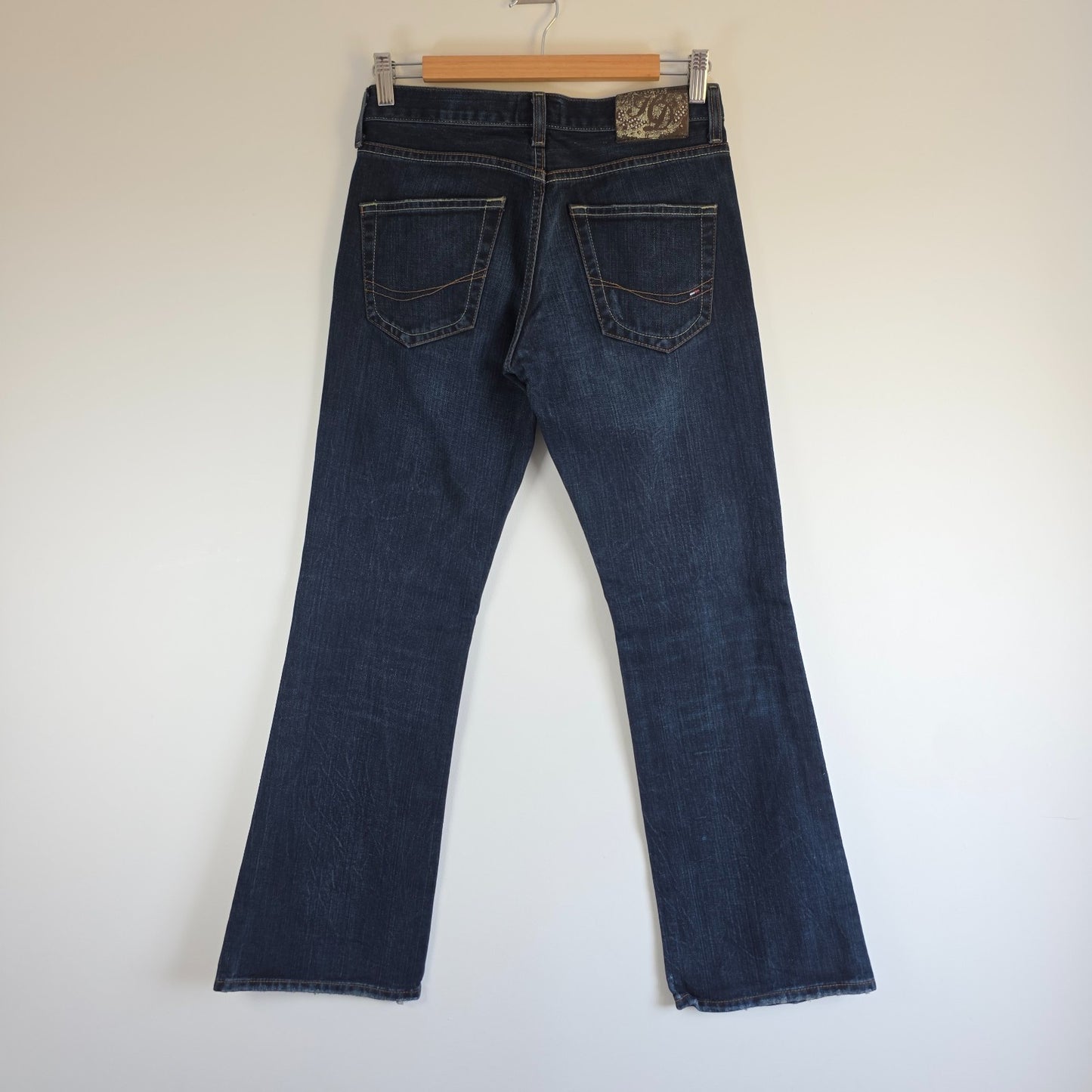 Tommy Hilfiger blue bootcut jeans with logo patch and classic denim texture.