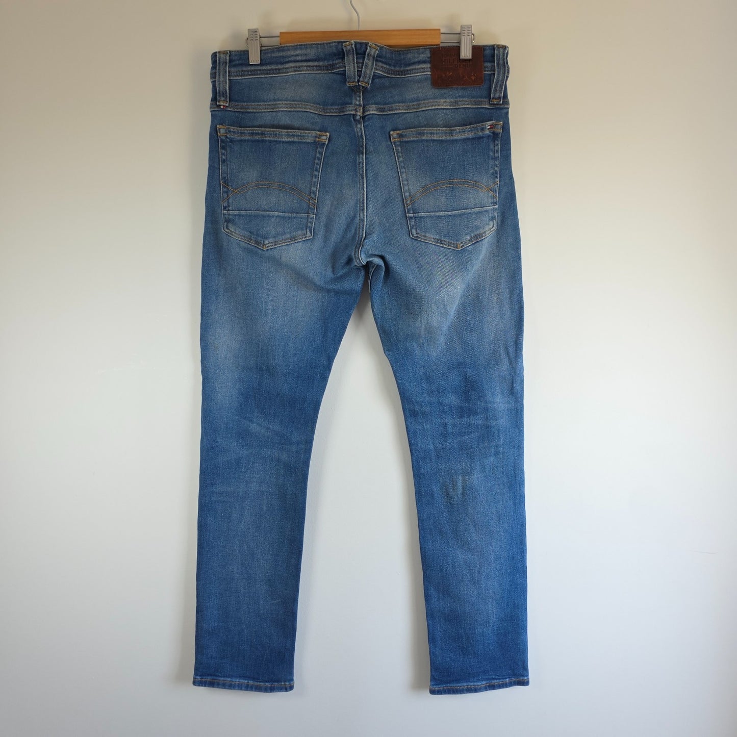 Tommy Hilfiger blue tapered jeans with stretch denim and small rip detail.
