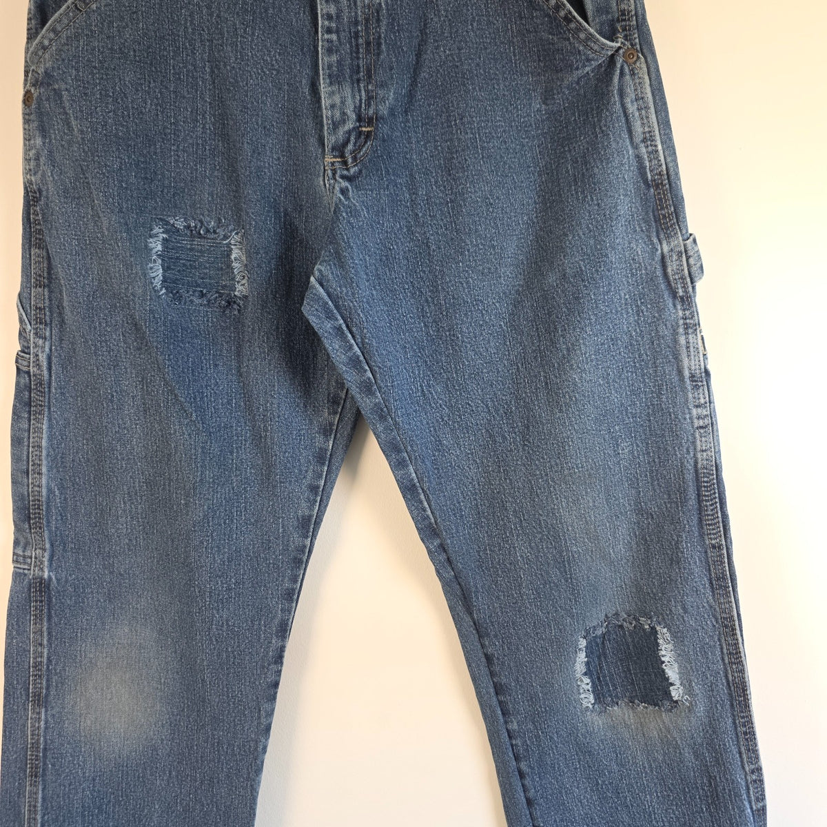 Wrangler blue carpenter jeans with distressed detailing, utility pockets, and hammer loop.